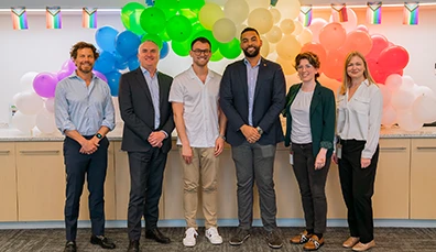 Business people standing in front of a rainbow balloon arch and pride flags