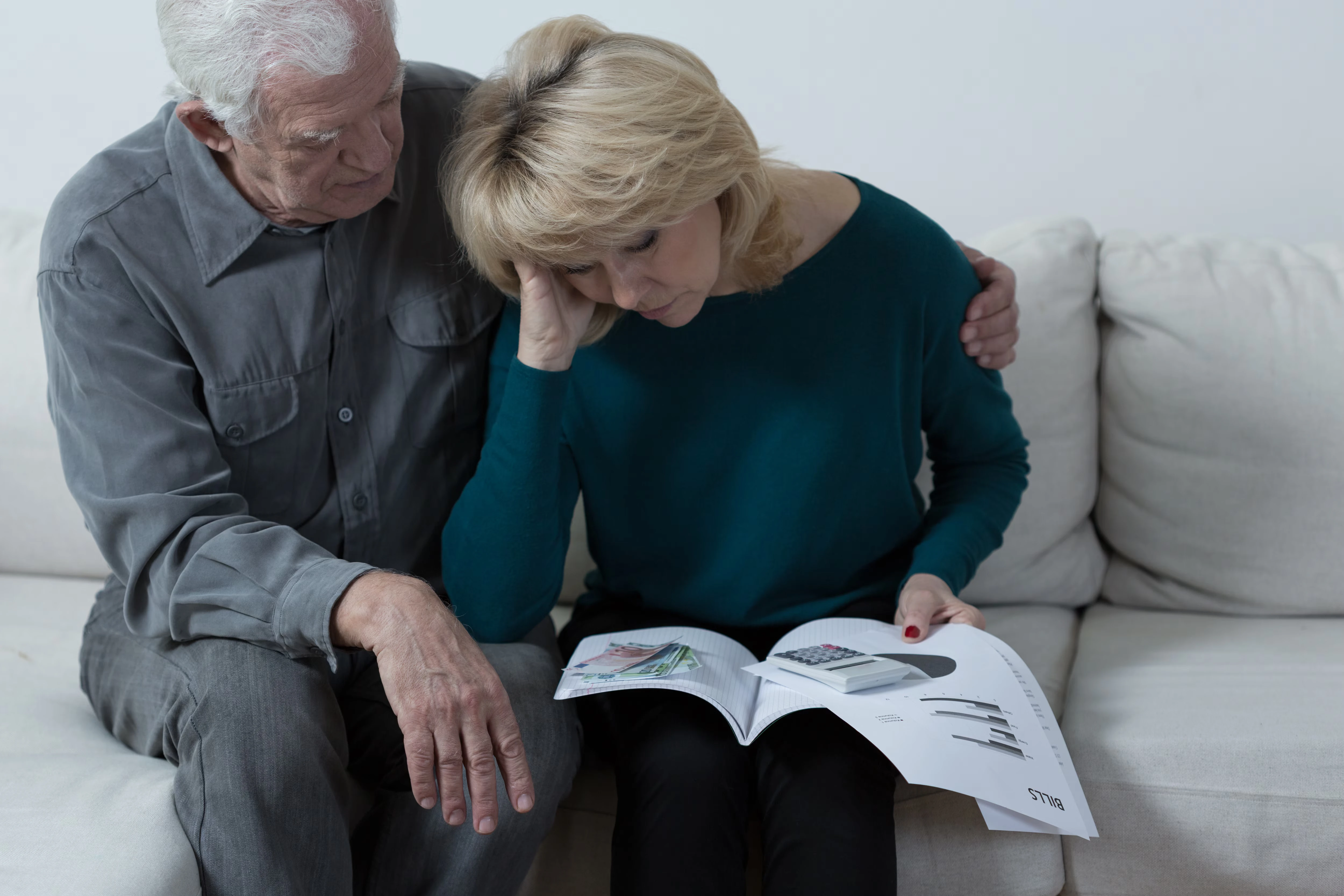 Older couple going over medical bills and paperwork. The woman is stressed and the man is trying to comfort her. 